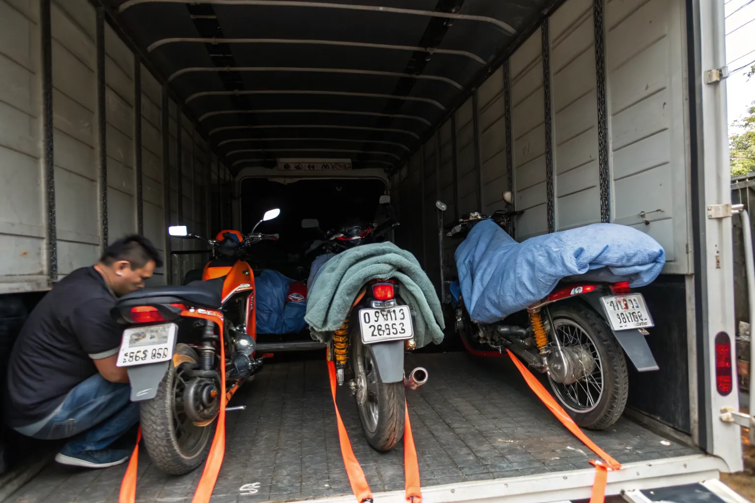 Motorcycles secured upright with ratchet straps and wheel chocks inside a covered box truck