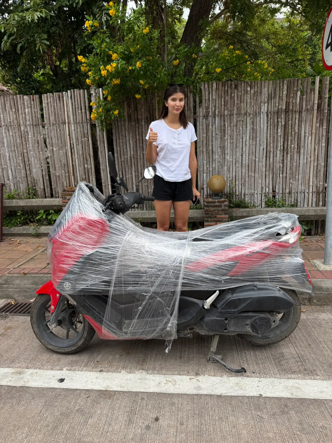 Customer giving a thumbs-up next to her shrink-wrapped Yamaha NMAX at delivery